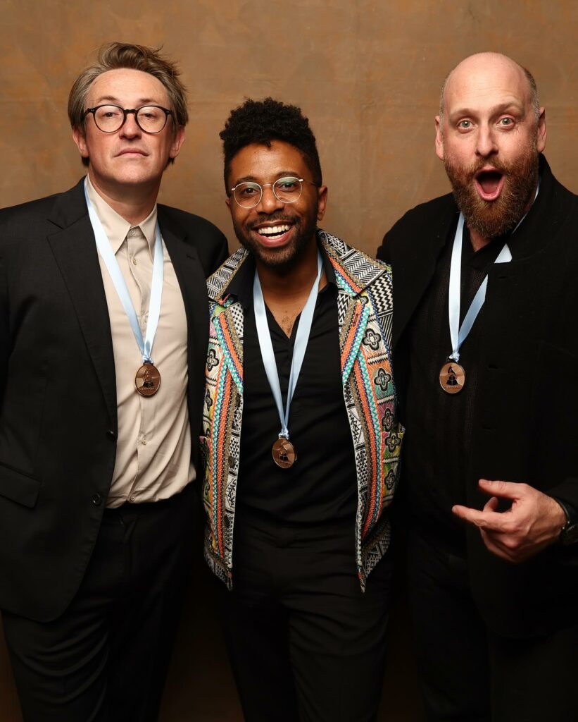 Three men wearing Grammy ribbons and smiling for the camera