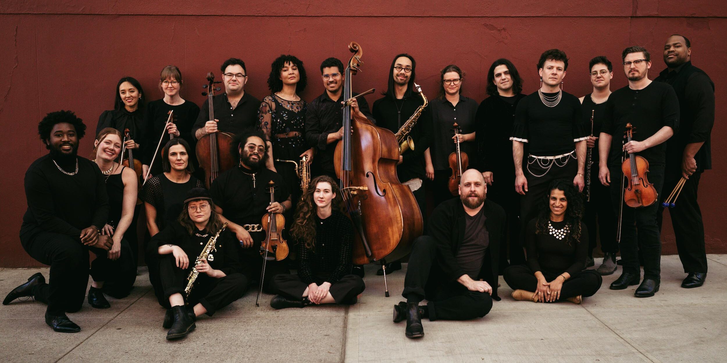 portrait of band members wearing all black holding their instruments against a brick wall